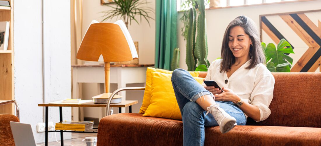 woman looks at housing maqrket update on her phone on the couch.