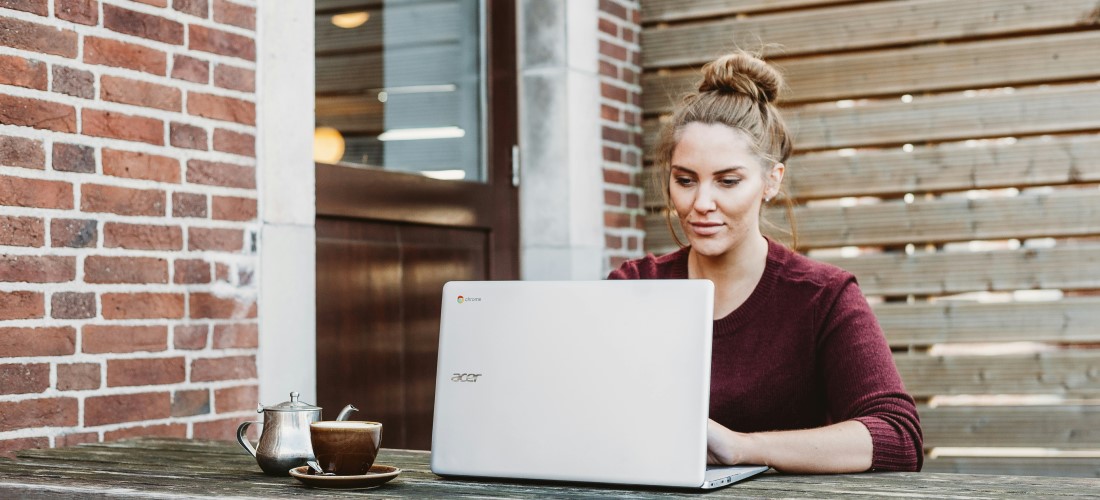 young woman sitting outside looking at the interest rate update on her laptop with a cup of tea.