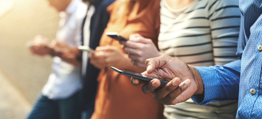 four people standing in a row holding their phones, checking their cybersecurity is up to date.